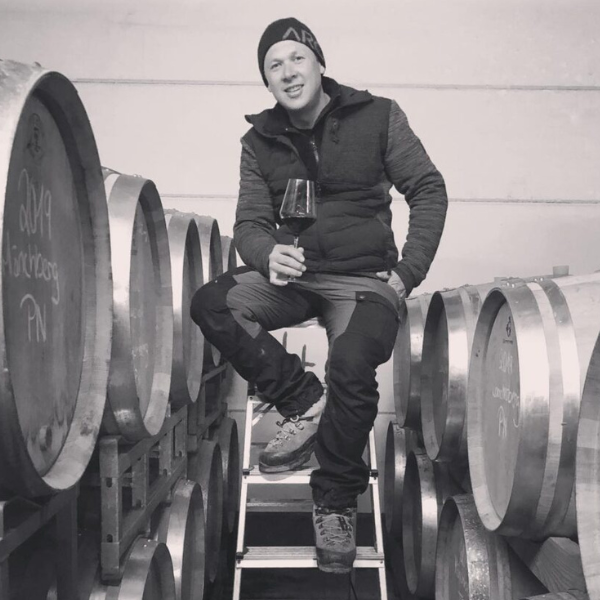 Zu sehen ist der Winzer Marc Josten mit einem Glas Wein in der Hand zwischen seinen Fässer-Wein und seinem Lager