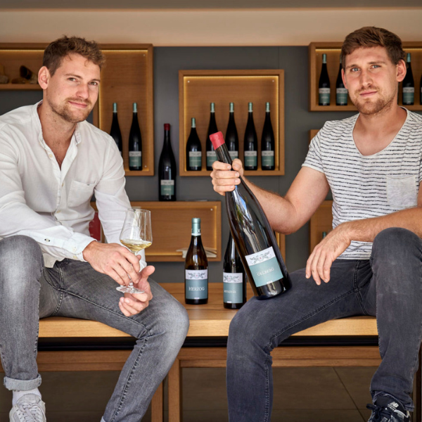 Nahaufnahme der zwei Winzer Michael und Thomas Andres, mit Weinglas und Weinflasche in der Hand