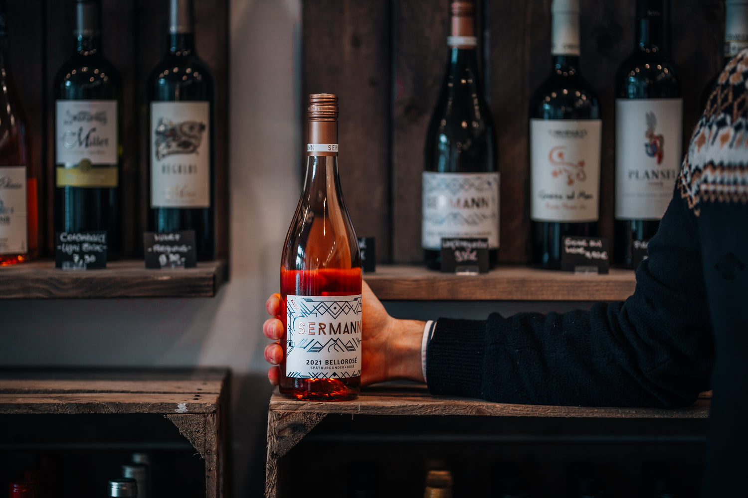 Im Fokus ist eine Roséflasche vom Weingut Sermann. Der Hintergrund zeigt weitere Flaschen in rustikalen Holzregalen