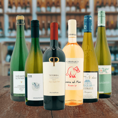 Ein elegantes Weinpaket bestehend aus den Lieblingsweinen der Vinothek Bonn. Zu sehen sind mehrere Flaschen Wein und Sekt. Im Hintergrund die Räumlichkeiten der Vinothek.